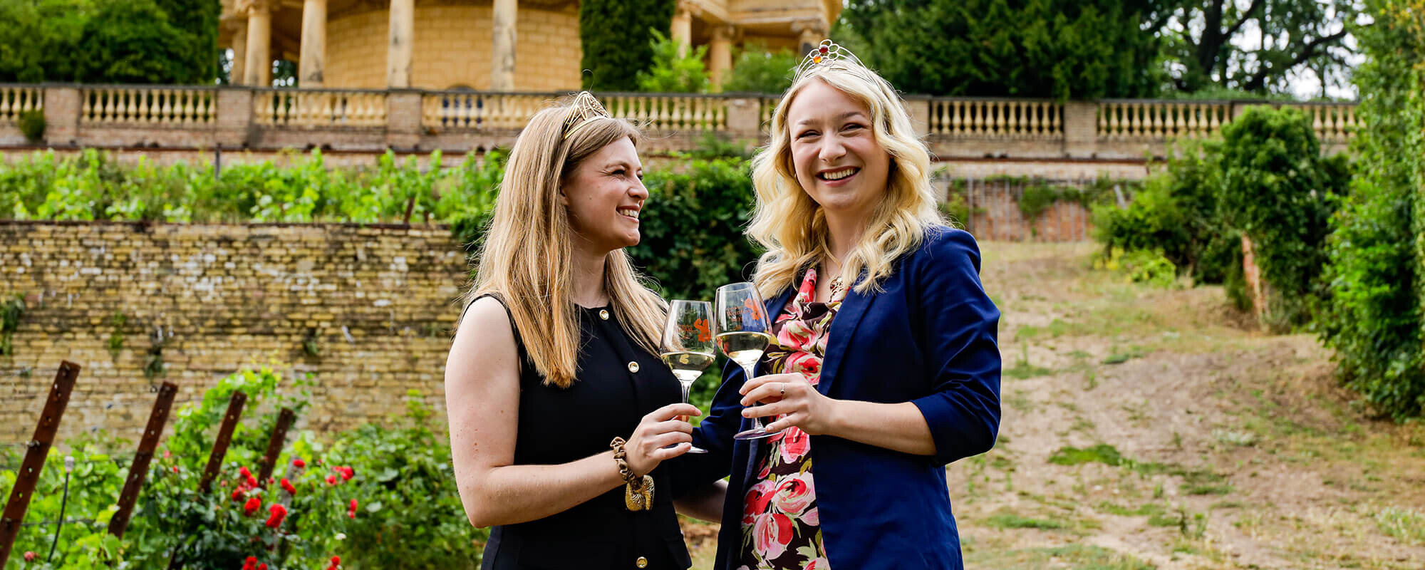 Zwei Weinköniginnen stoßen auf dem Königlichen Weinberg zusammen mit Weißwein an